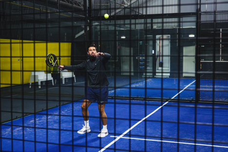 Padelspeler die speelt een hoge bal over het net heen naar de overkant van de padelbaan