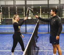 Twee padelspelers op een padelbaan van Padelclub Nederland locatie Druten die elkaar feliciteren over het net heen